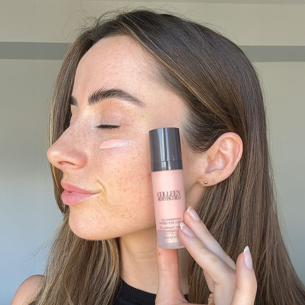 Woman with Illuminating Tinted Eye Cream swatch on cheek and bottle.