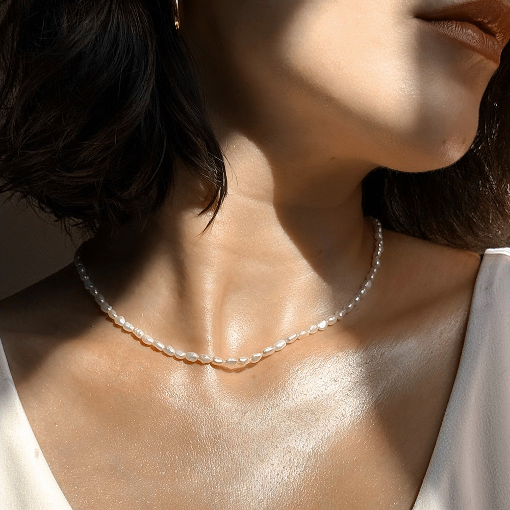 Close-up of a person wearing a pearl necklace wearing the Ethereal Glow Serum on face and neck.