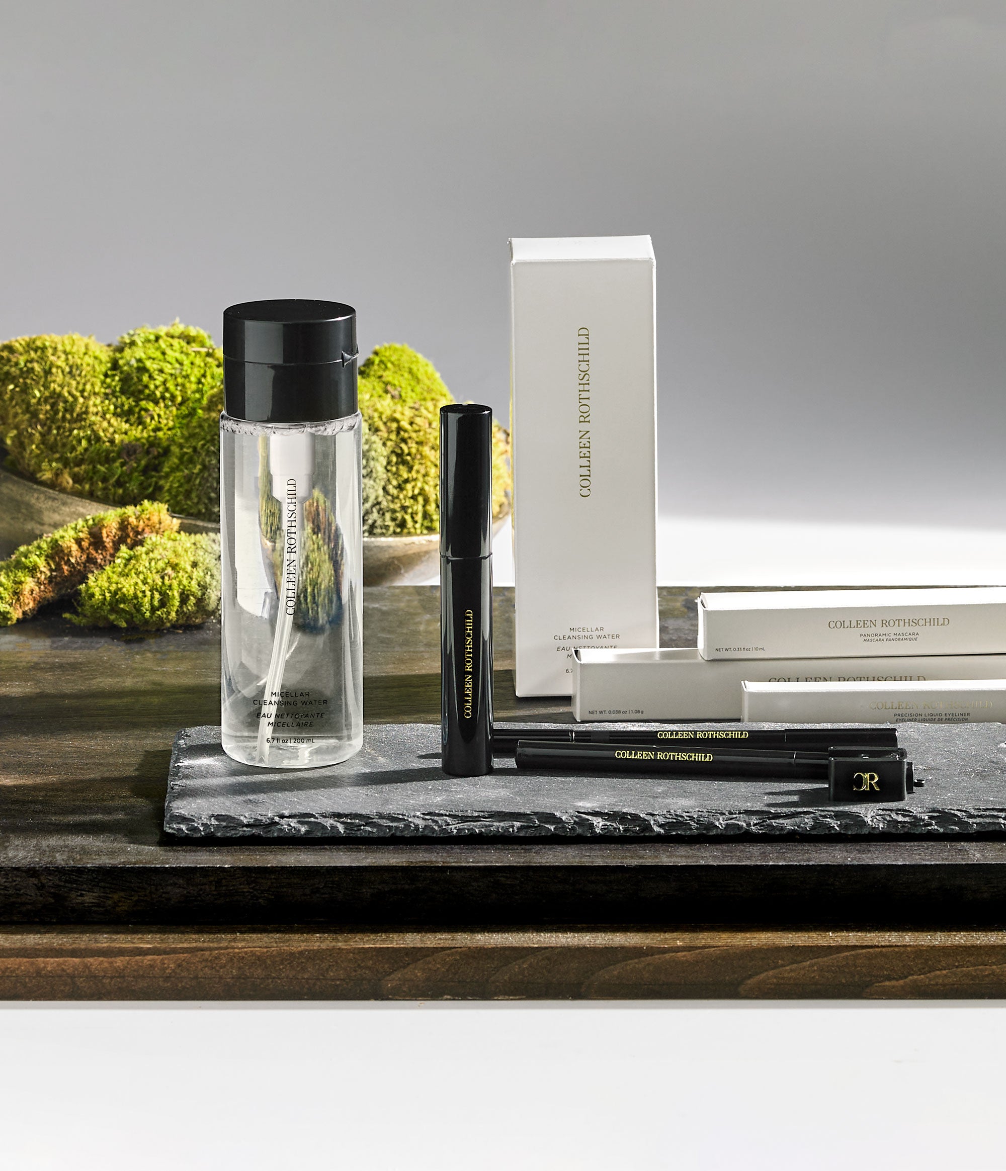 Colleen Rothschild Beauty Micellar Cleansing Water, mascara, and eyeliner displayed on a slate surface with a natural moss backdrop.