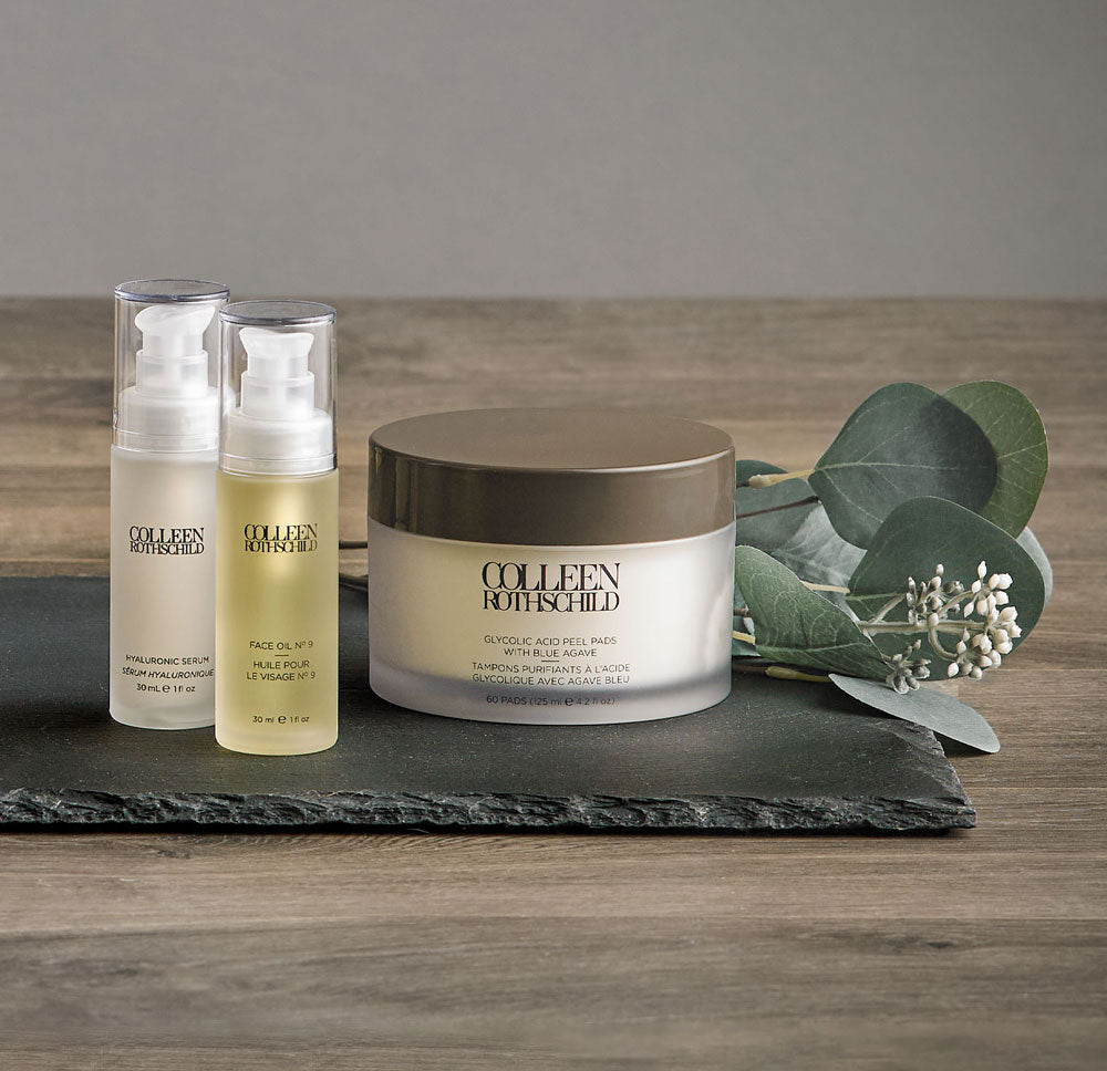 Skincare bottles and jar on slate with plant.